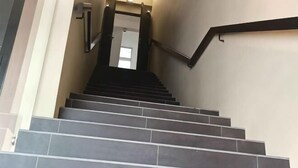 Μια σκάλα με σκούρα γκρι σκαλοπάτια και μαύρες μπάρες στήριξης, που οδηγεί σε έναν εσωτερικό χώρο.