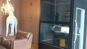 Ένα δωμάτιο με ένα γυάλινο διαχωριστικό, ένα λευκό γλυπτό ζιράφας, έναν καφέ δερμάτινο καναπέ και ένα πολυέλαιο.