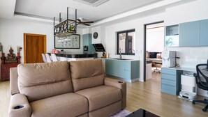 A modern living room with a beige sofa, a kitchen area with light blue cabinets, and a dining area with a wooden table. - Tilawan Villa - Cozy 3 Bedrooms Pool Villa in Chalong (Chang Wat Phuket)