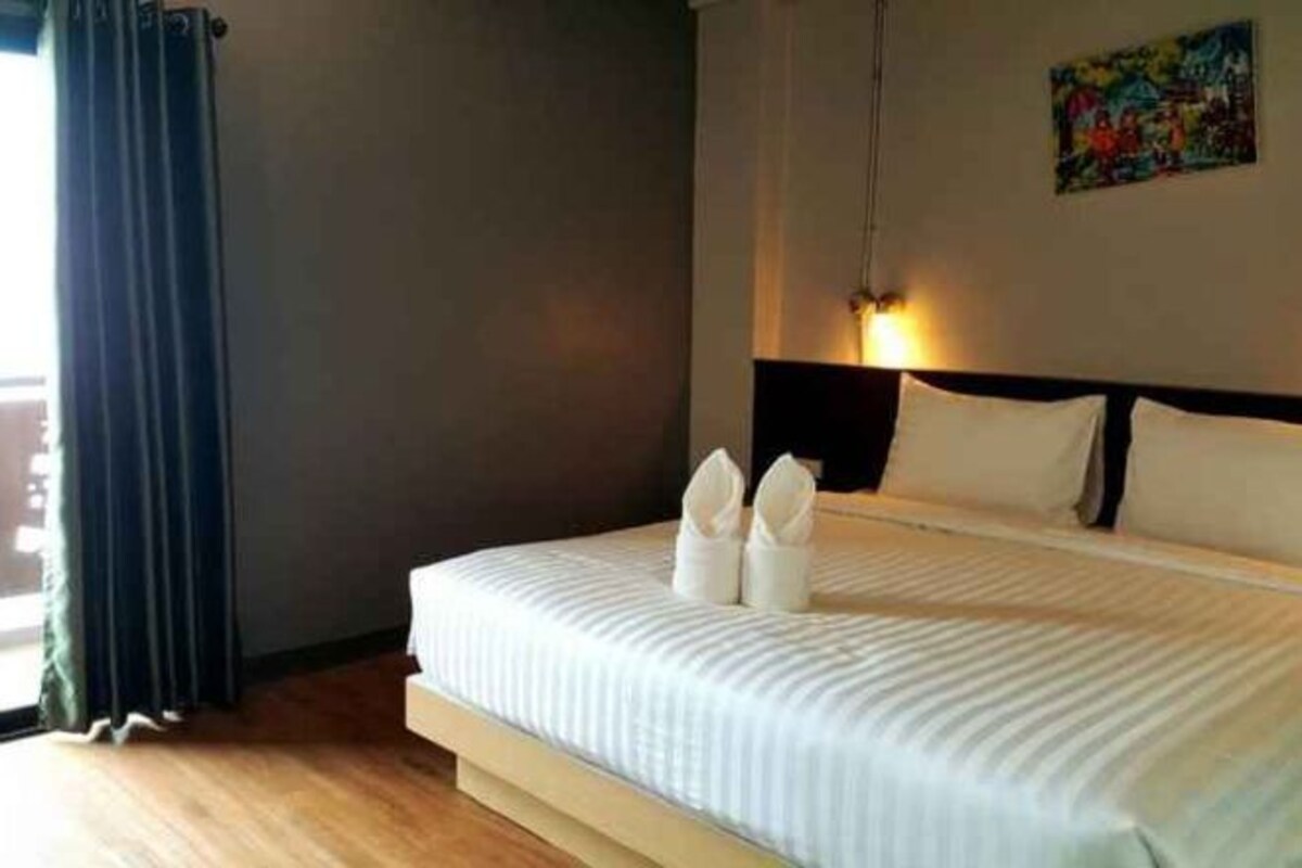 A hotel room with a bed, a painting on the wall, and a window with curtains.