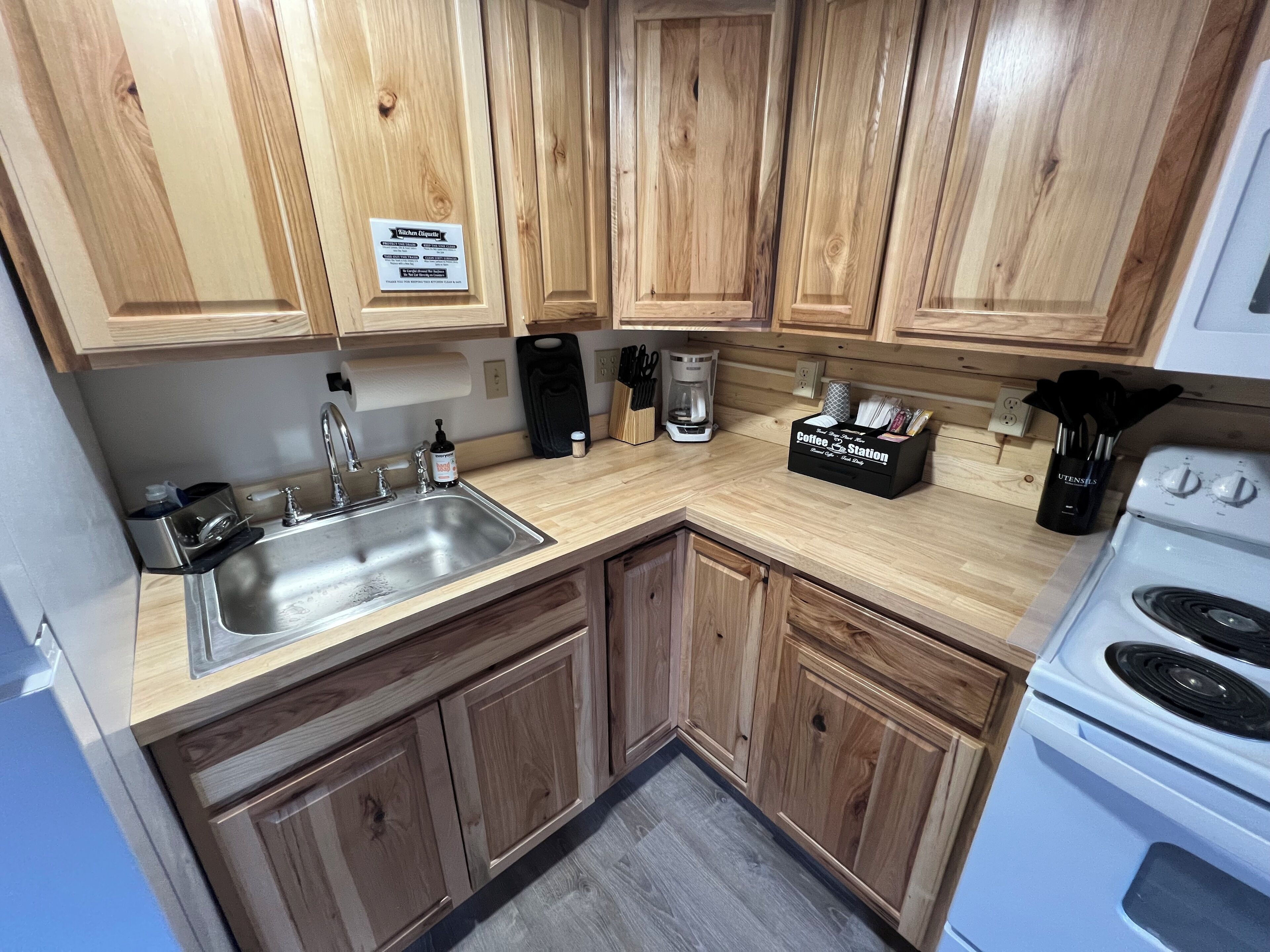 A kitchen with wooden cabinets, a stainless steel sink, a coffee station, and a white stove.