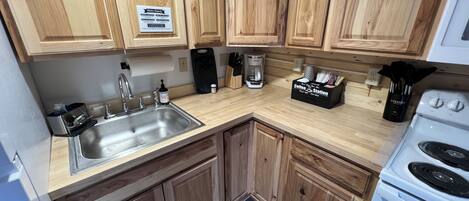A kitchen with wooden cabinets, a stainless steel sink, a coffee station, and a white stove.