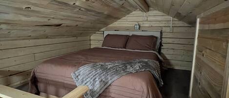 A wooden cabin room with a bed, a small table, and a wooden railing.