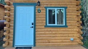 Eine Blockhütte mit einer weißen Tür, einem kleinen Fenster und einer Fußmatte.
