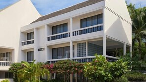 Een hotel met meerdere verdiepingen, balkons, een plat dak en weelderige begroeiing eromheen.