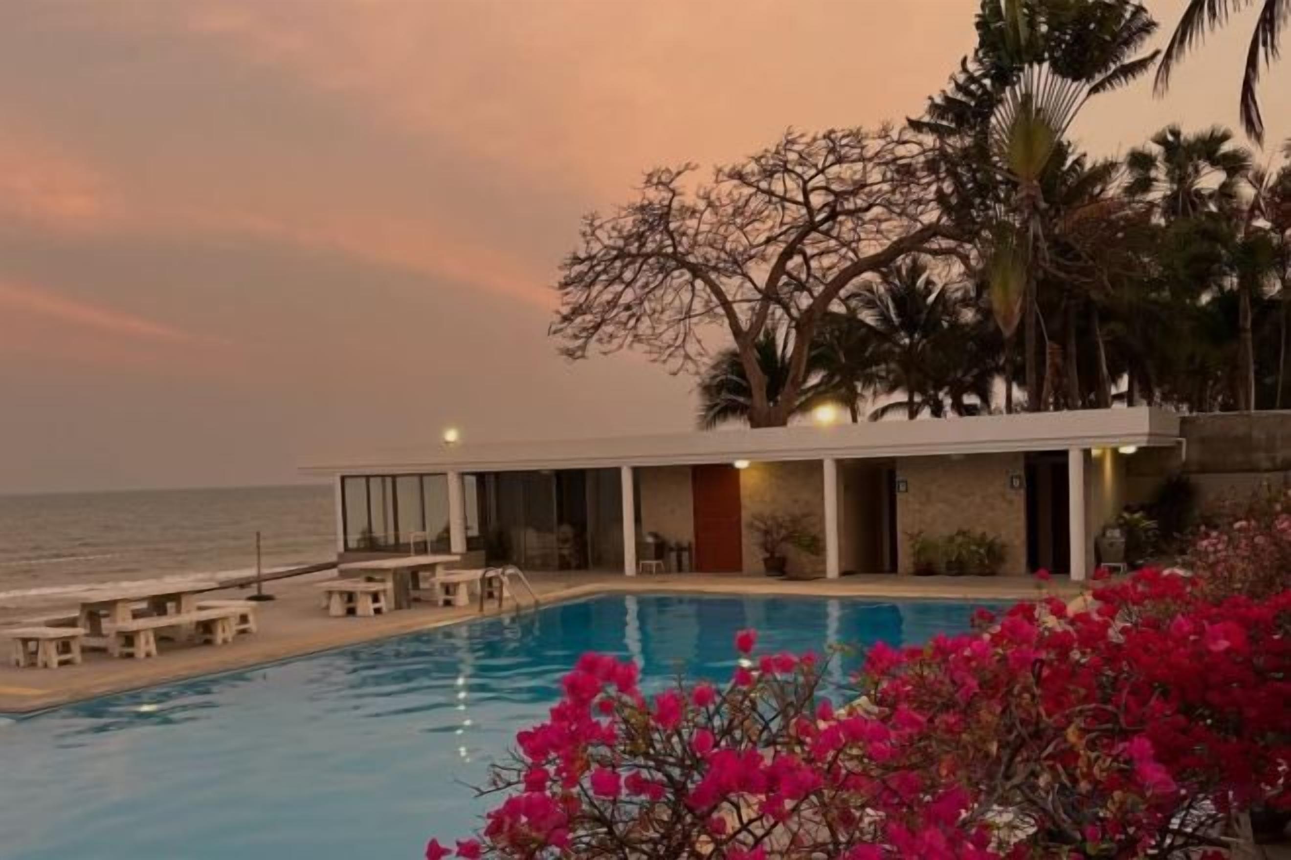 A poolside view of a hotel with a pool, lounge chairs, and a view of the ocean.