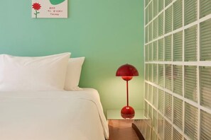 Una cama con ropa blanca, una lámpara de pie roja y una pared verde con una ventana.