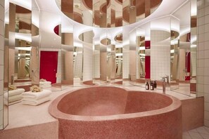 A modern bathroom with a large circular bathtub, multiple mirrors, and a red accent wall. - Molly Beach House by Yudee Assets (Hua Hin)