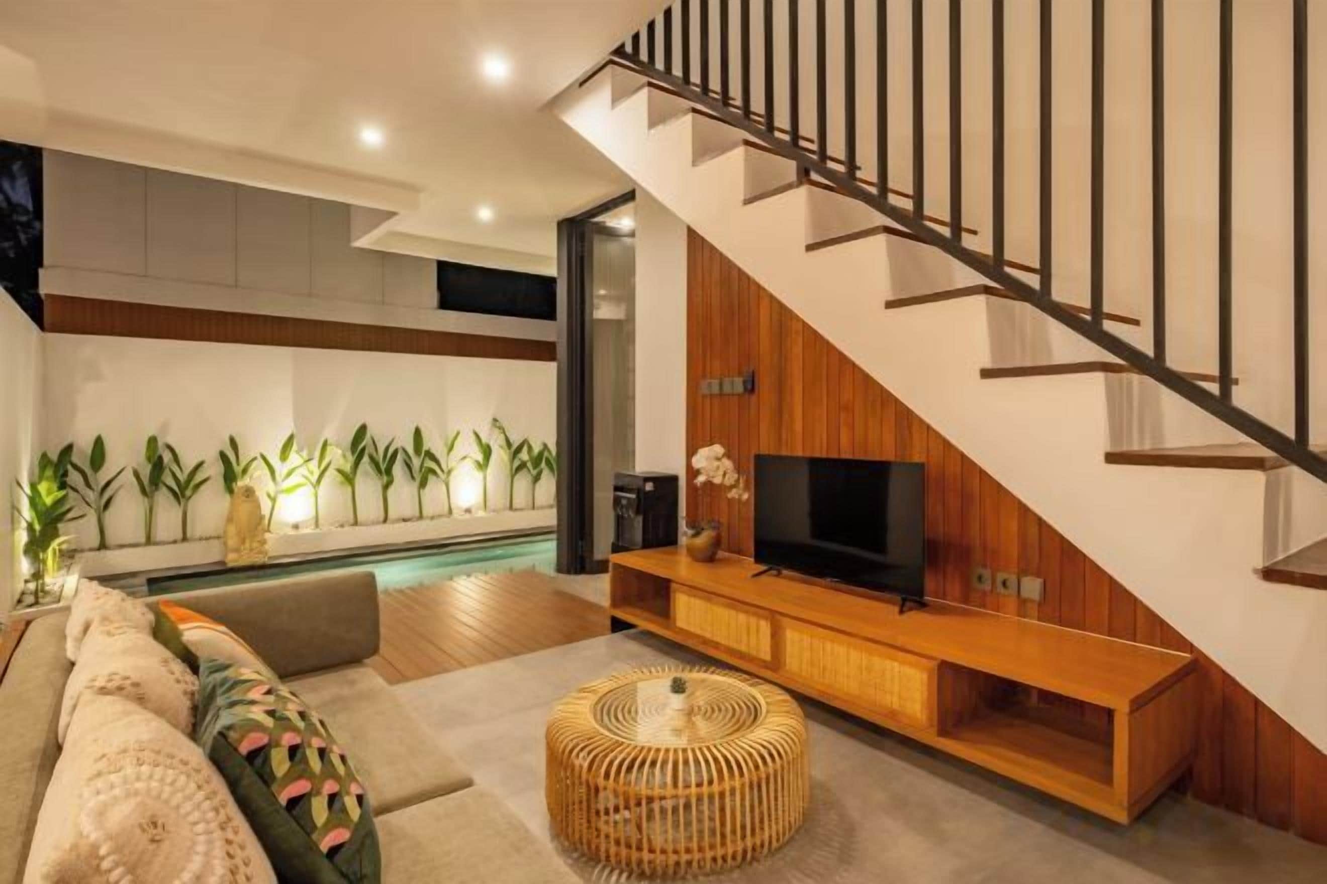 A modern living room with a staircase, a flat-screen TV, and a pool area.