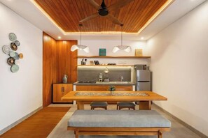Une cuisine moderne avec des meubles en bois, une table à manger avec des chaises et des luminaires suspendus.