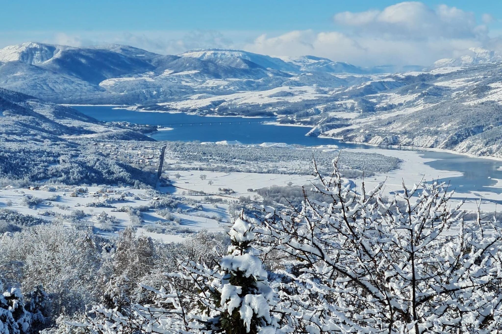 A snowy landscape with a lake, mountains, and a bridge.