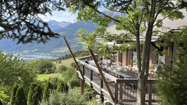 Eine Holzterrasse mit Sitzgelegenheiten im Freien mit Blick auf eine Berglandschaft und einen See.