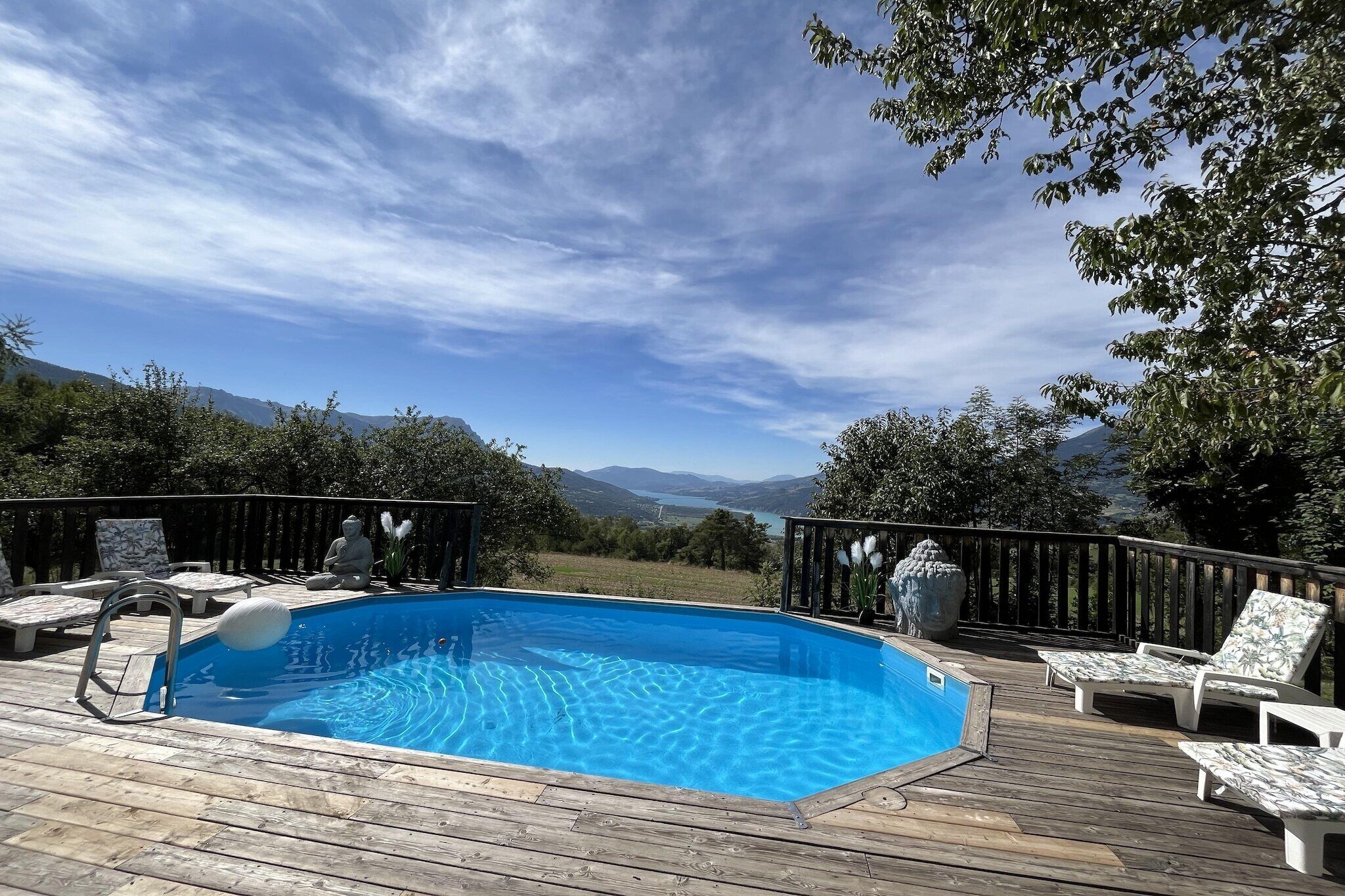 Une terrasse en bois avec une piscine, des chaises longues et une vue imprenable sur les montagnes.
