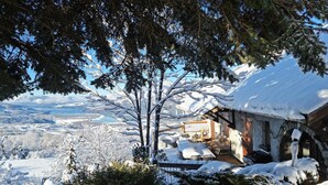 Ein mit Schnee bedecktes Holzhäuschen in den Bergen mit Veranda und Blick auf eine verschneite Landschaft.