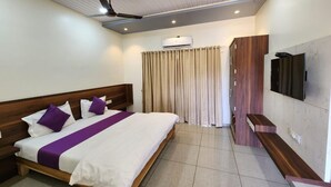 Habitación de hotel con cama, televisor, aire acondicionado y ventilador de techo.