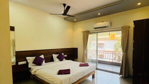 Habitación de hotel con cama, ventilador de techo, aire acondicionado y vista al exterior a través de un ventanal grande.