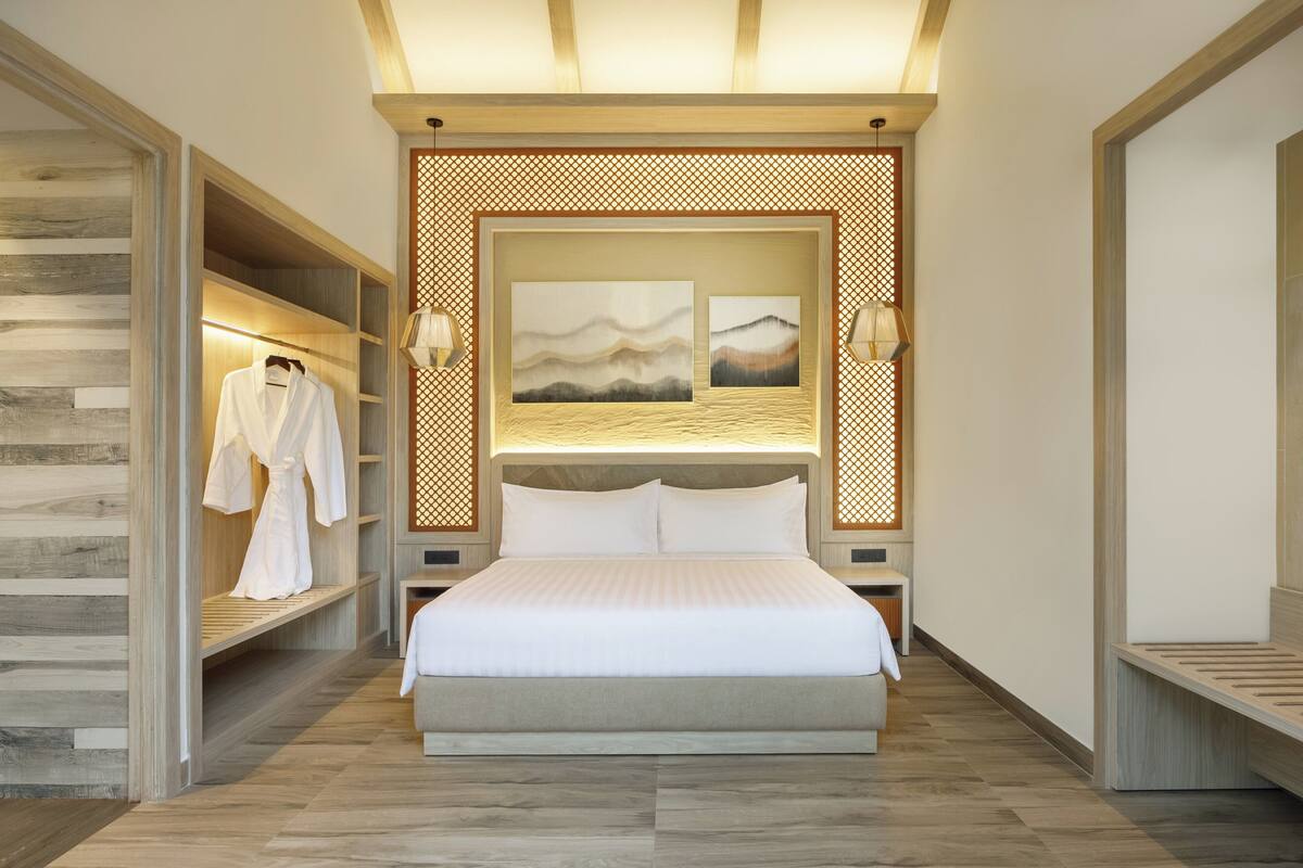 A modern hotel room with a large bed, wooden shelving, and artwork on the headboard.