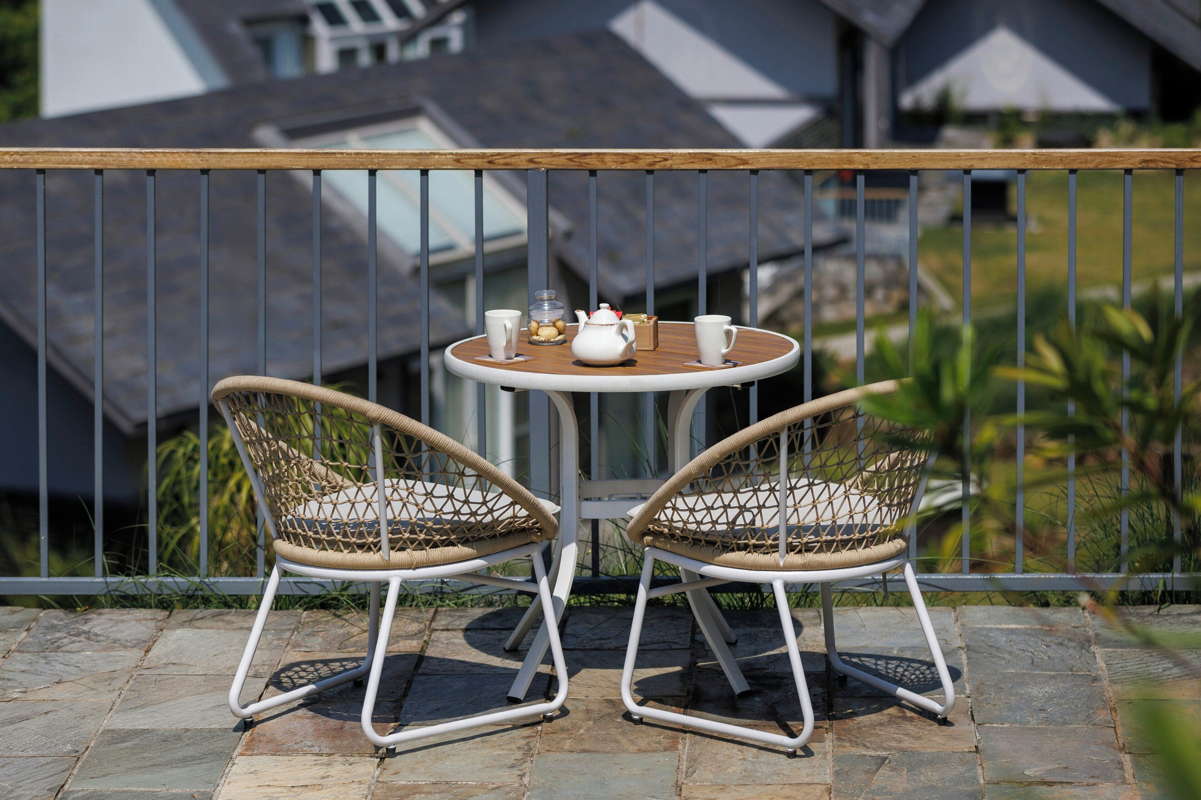 A balcony with two wicker chairs, a small round table, and a white teapot.