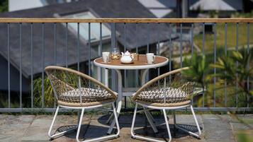 A balcony with two wicker chairs, a small round table, and a white teapot.