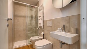 Egy modern fürőszoba, melyben üvegfalas zuhanyzó, WC és mosdókagyló található, a mosdókagyló felett pedig tükör van.