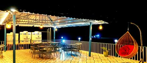 An outdoor patio with tables and chairs, a hanging chair, and a covered area with a roof.