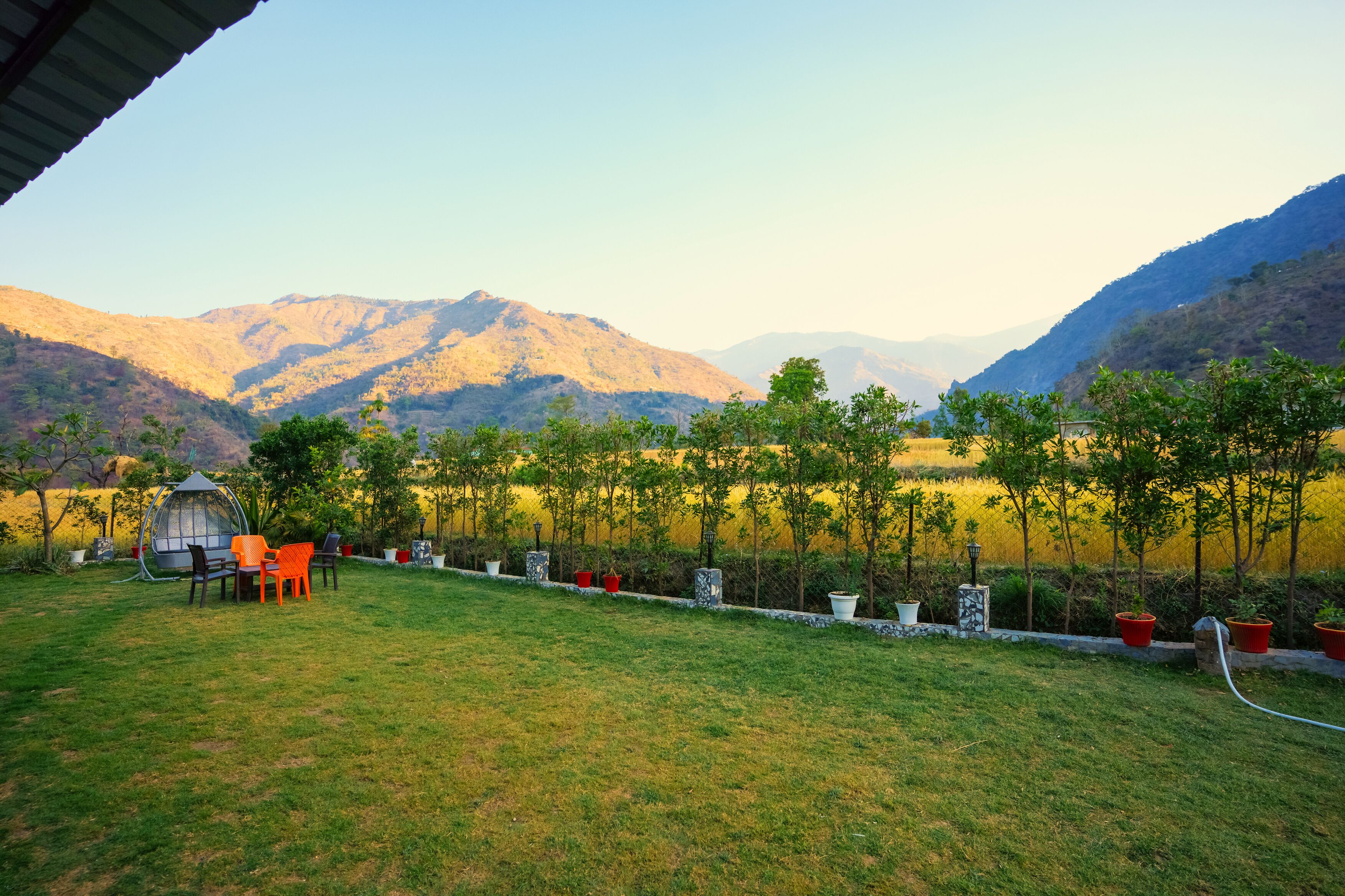 A grassy outdoor area with a table and chairs, potted plants, and a view of mountains.