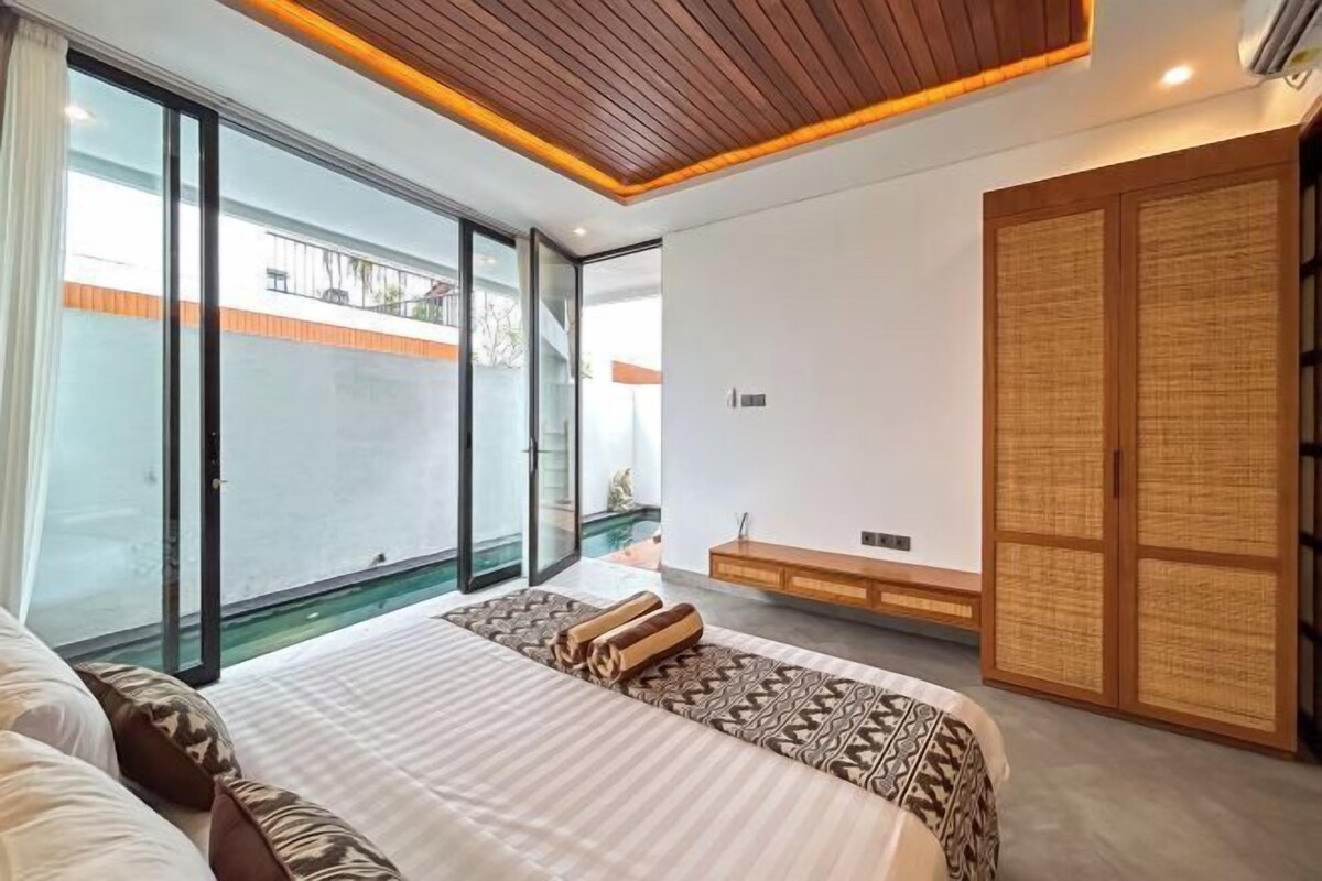 A modern bedroom with a large bed, a sliding glass door to a balcony, and a traditional wooden wardrobe.