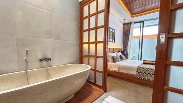 A modern bathroom with a freestanding bathtub, a wooden floor, and a large window providing natural light. - Villa Sudut Padi Ubud (Bali)