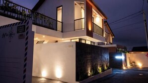 A modern two-story house with a balcony, a well-lit entrance, and a landscaped garden area. - Villa Sudut Padi Ubud (Bali)