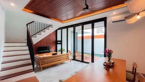 A modern living room with a wooden staircase, a dining table, and a TV. - Villa Sudut Padi Ubud (Bali)