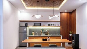A modern kitchen with a dining area, wooden cabinets, a refrigerator, and pendant lighting. - Villa Sudut Padi Ubud (Bali)