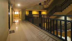 A corridor with a tiled floor, a black railing, and a staircase with a black handrail. - San Marino JY7 Rentals by RedDoorz (Cebu City)