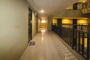 A corridor with a tiled floor, a railing on one side, and doors on the other.