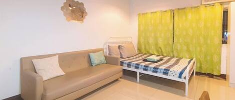 Una habitación con sofá, cama con colcha estampada, lámpara de pared y cortina verde.