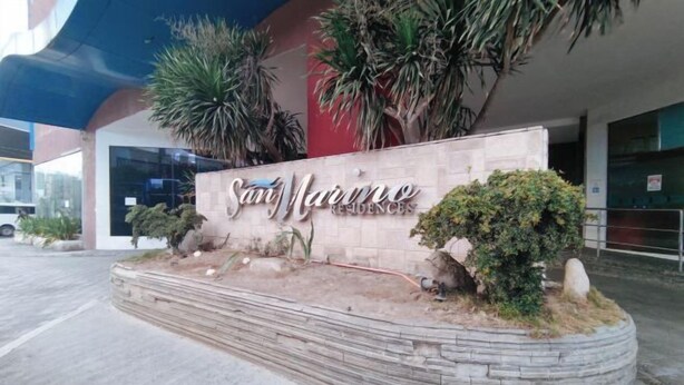 A sign for San Marino Residences with a landscaped area featuring plants and a stone border. - San Marino JY7 Rentals by RedDoorz (Cebu City)