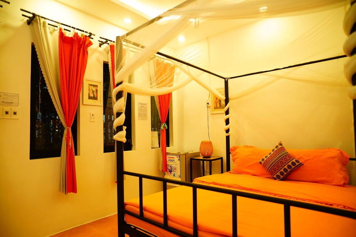 Una habitación con una cama con dosel, cortinas rojas y una mesita de noche con lámpara.