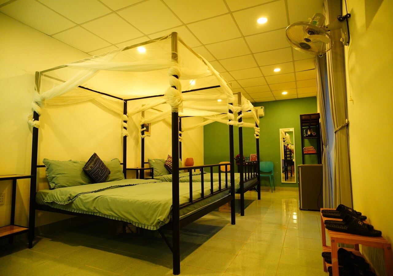 A four-poster bed with a canopy, a small table, and a chair in a room with green walls and a tiled floor.