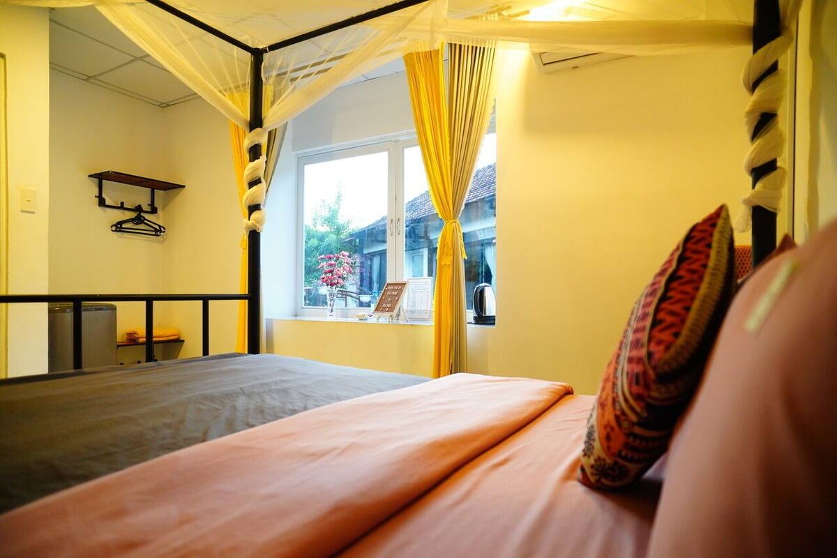 Una cama con dosel, una ventana con cortinas y vistas al exterior.
