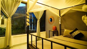 A room with a bed, curtains, a small table, and a wall-mounted mirror. - Vuon Thu Do Homestay (Buon Ma Thuot)