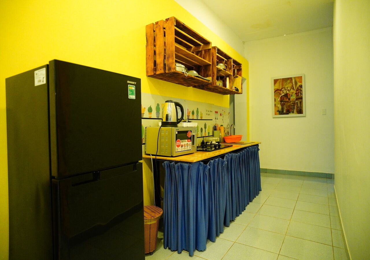 A compact kitchen with a black refrigerator, a wooden shelf above the counter, and a blue curtain covering the table.