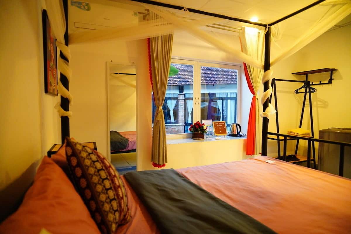 Un dormitorio con cama, una ventana con cortinas, una mesita y una silla.