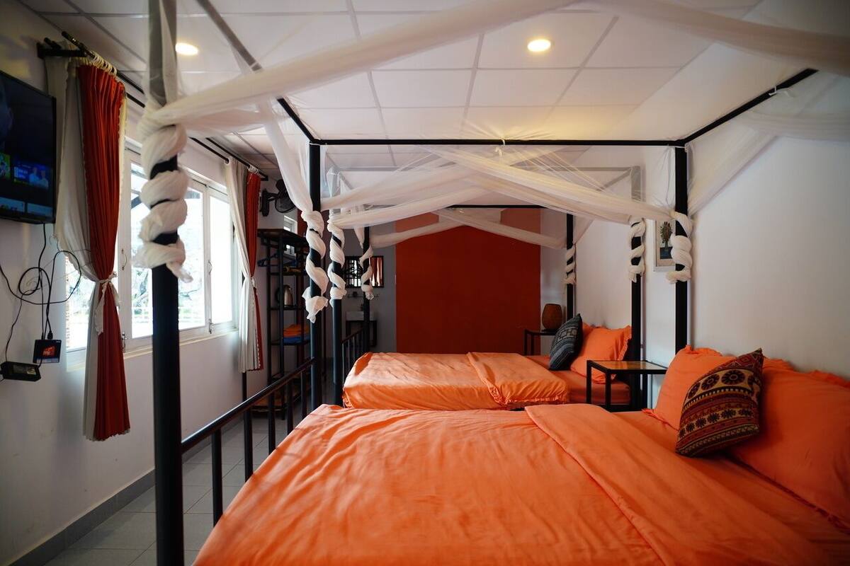Una habitación con dos camas, ropa de cama naranja, un dosel blanco y una pared de acento roja.