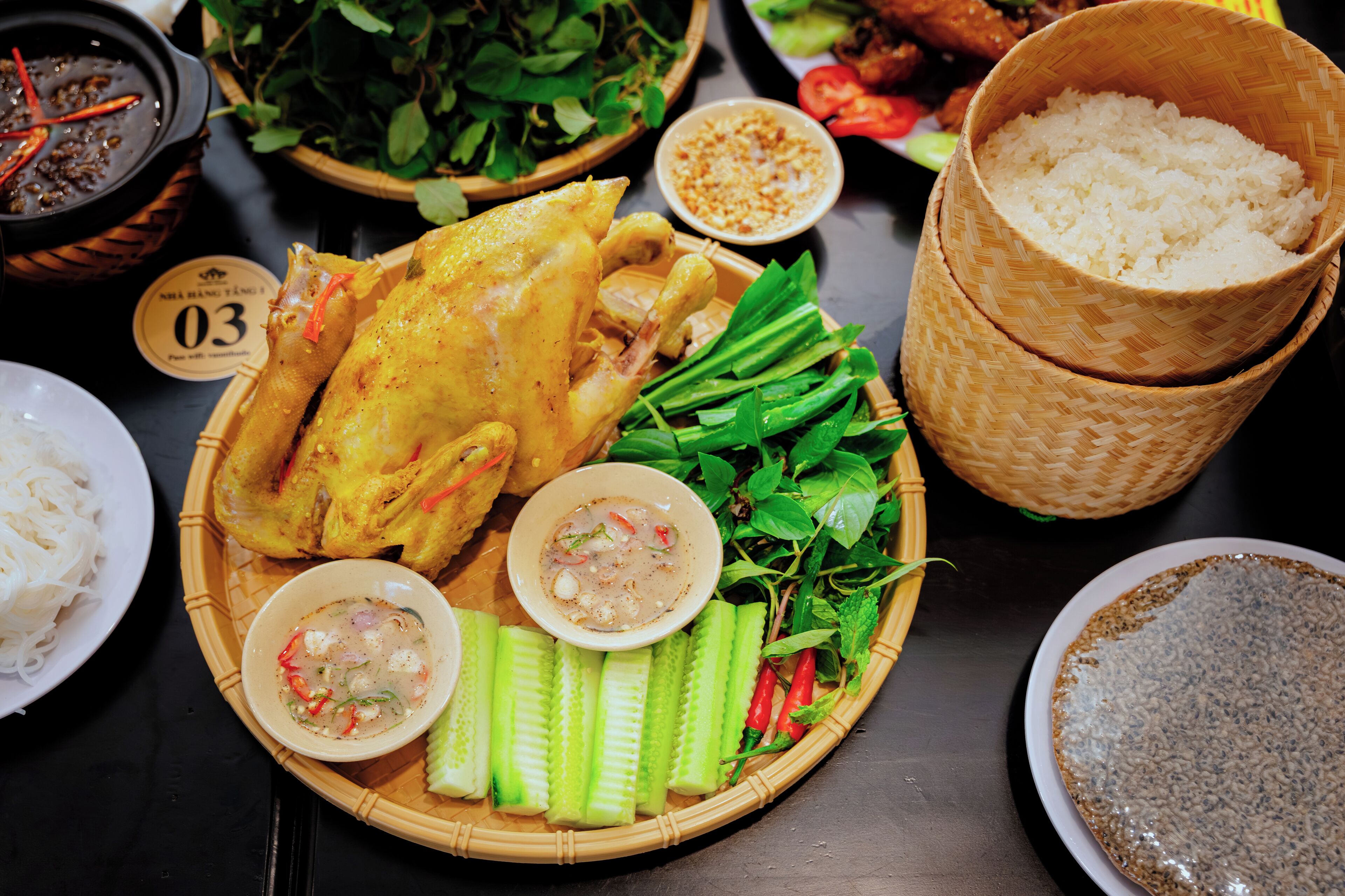 A table with a variety of dishes including a whole roasted chicken, fresh vegetables, and rice.