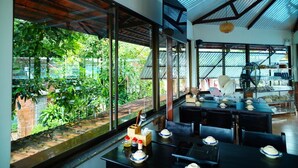 A restaurant with large windows, a dining area, and a view of greenery outside. - Vuon Thu Do Homestay (Buon Ma Thuot)
