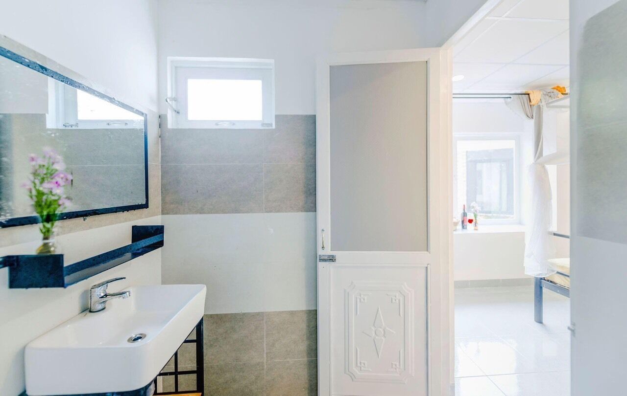 Une salle de bain moderne avec un lavabo blanc, un miroir et une porte donnant sur l’espace douche.