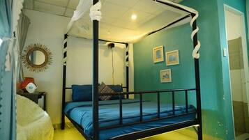 Una cama con dosel y dos columnas, una mesita de noche con lámpara y un espejo fijado a la pared.