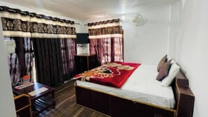 A bedroom with a bed, curtains, a bedside table, and a wall-mounted fan. - Hotel Dreamland (Udhampur)
