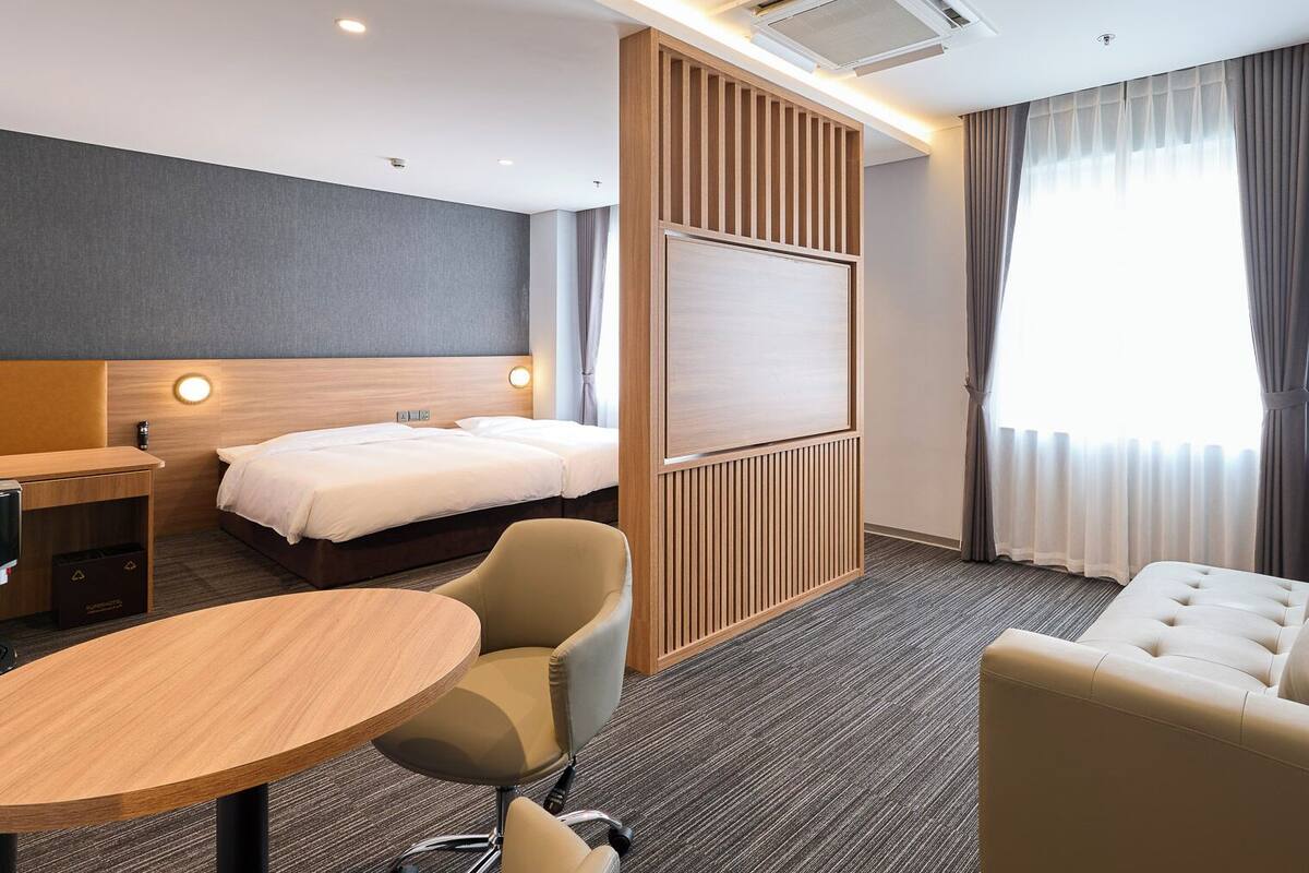 Una habitación de hotel con una cama, un escritorio, una mesa redonda, un sofá y un ventanal con cortinas.