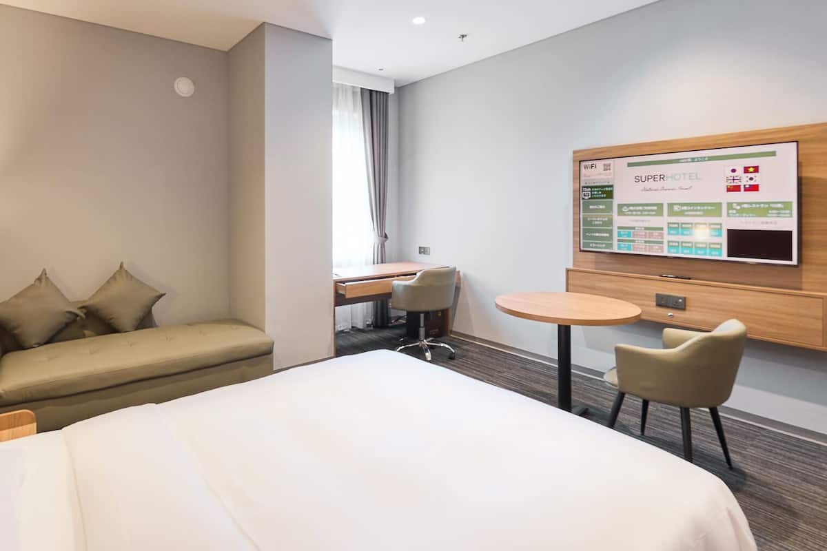 Habitación de hotel con cama, sofá, escritorio, silla y televisor que muestra información del hotel.