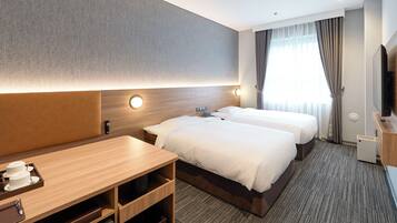 Ein Hotelzimmer mit zwei Betten, einem Schreibtisch mit Kaffeemaschine, einem Fernseher und einem großen Fenster mit Vorhängen.